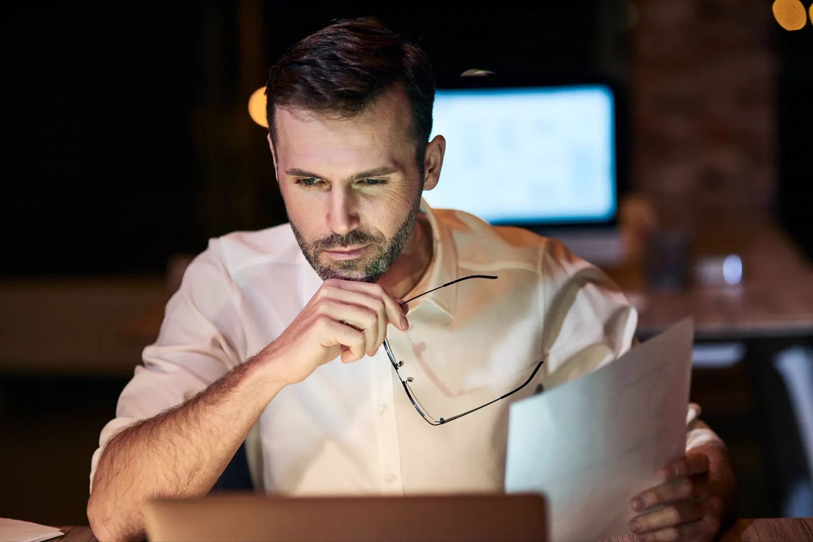 Business owner reviewing a printed report at a laptop late in the evening.