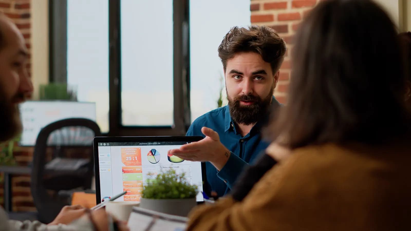 Business professional presenting analytics and charts on a laptop during a team meeting.